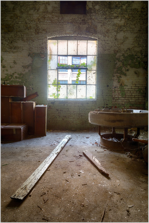 An abandoned space with a dusty floor, wooden beams, and a window surrounded by creeping vines.