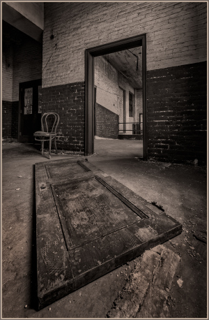 A warped door rests on the floor, framing a shadowy archway. A solitary chair whispers of forgotten tales and time's emb