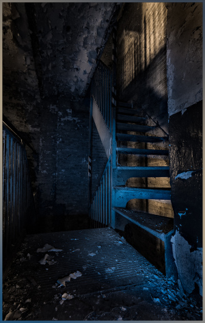 Interior staircase with shadows and blue light, highlighting historical elements of the structure.