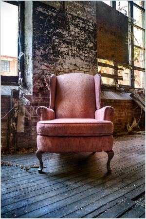A worn pink chair in a dusty, dilapidated space; layers of peeling paint.