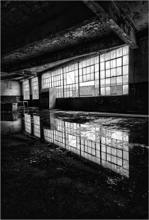 Gloomy interior with large windows casting reflections on the water.