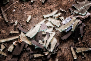 Shattered glass pieces scattered on a dusty surface, remnants of a forgotten space.