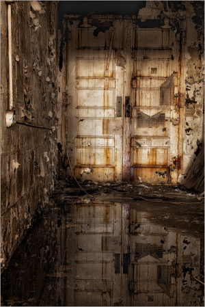 Rusty doors stand guard, reflections dance on puddles.