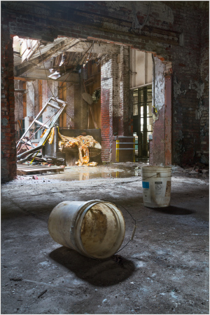 A desolate space with buckets scattered on cracked floors, remnants of past life linger in stillness.