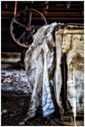 A weathered fabric drapes over a rusted structure, with shadows playing in the dim light.