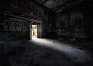 Dark, abandoned space with graffiti on walls, shadows creeping through a doorway.