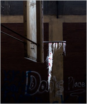 A broken window draped with threads of white and red against a backdrop of faded graffiti.