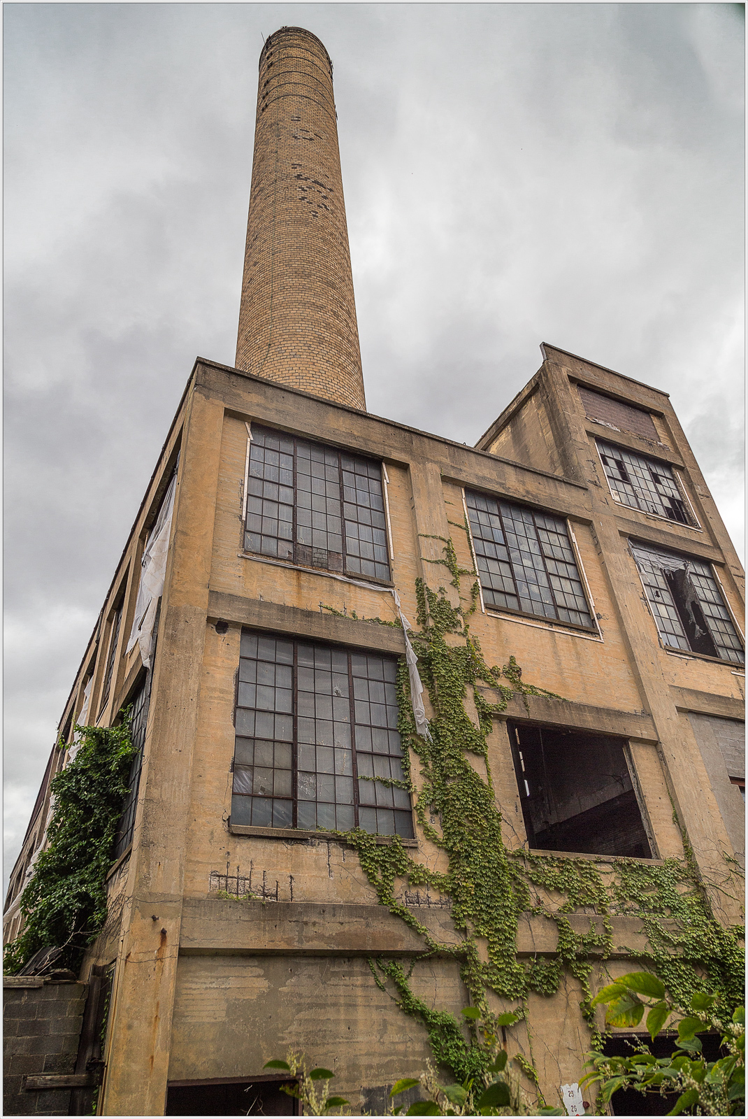 An abandoned industrial building with a tall smokestack and ivy creeping up its walls.