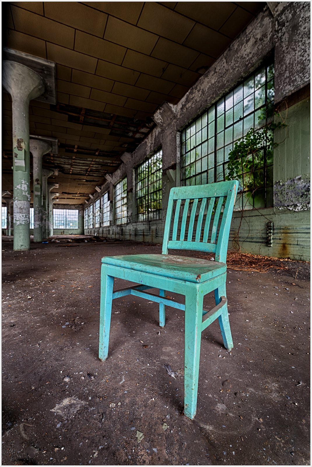 A quirky turquoise chair stands alone in a spacious, worn-out industrial room.