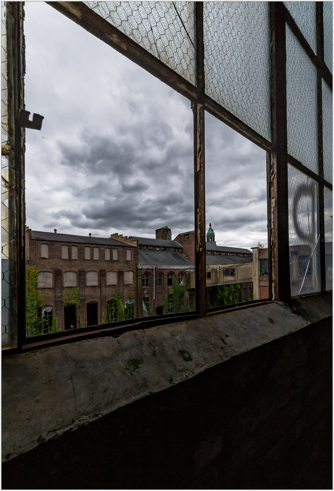 A view through a weathered window, framing a somber landscape of brick and sky.