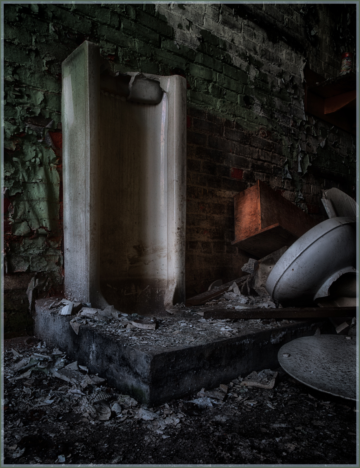 An abandoned shower stall amidst crumbling walls and scattered debris.