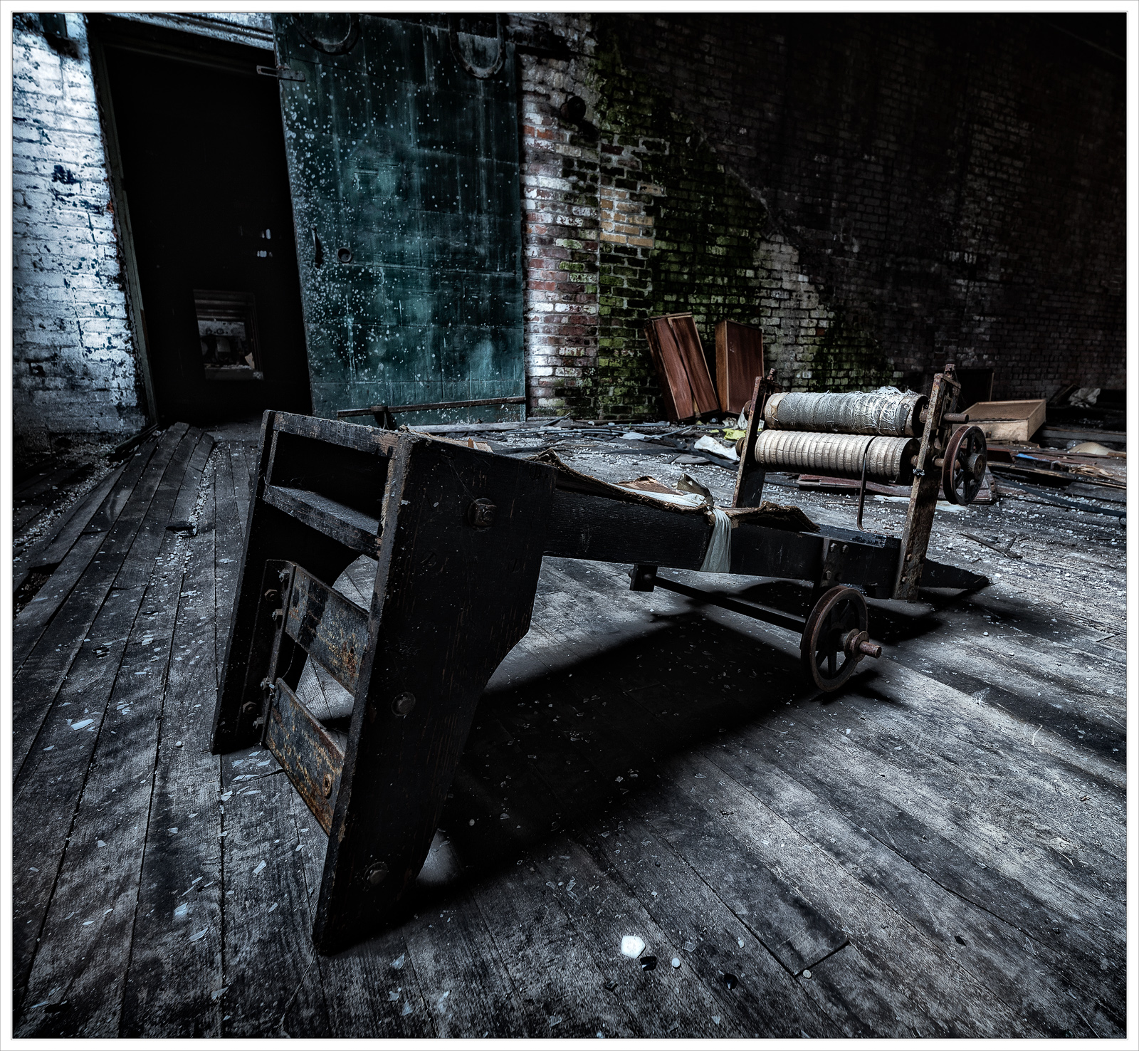 A haunting apparatus with wheels sits abandoned on a dusty floor, cloaked in shadows.