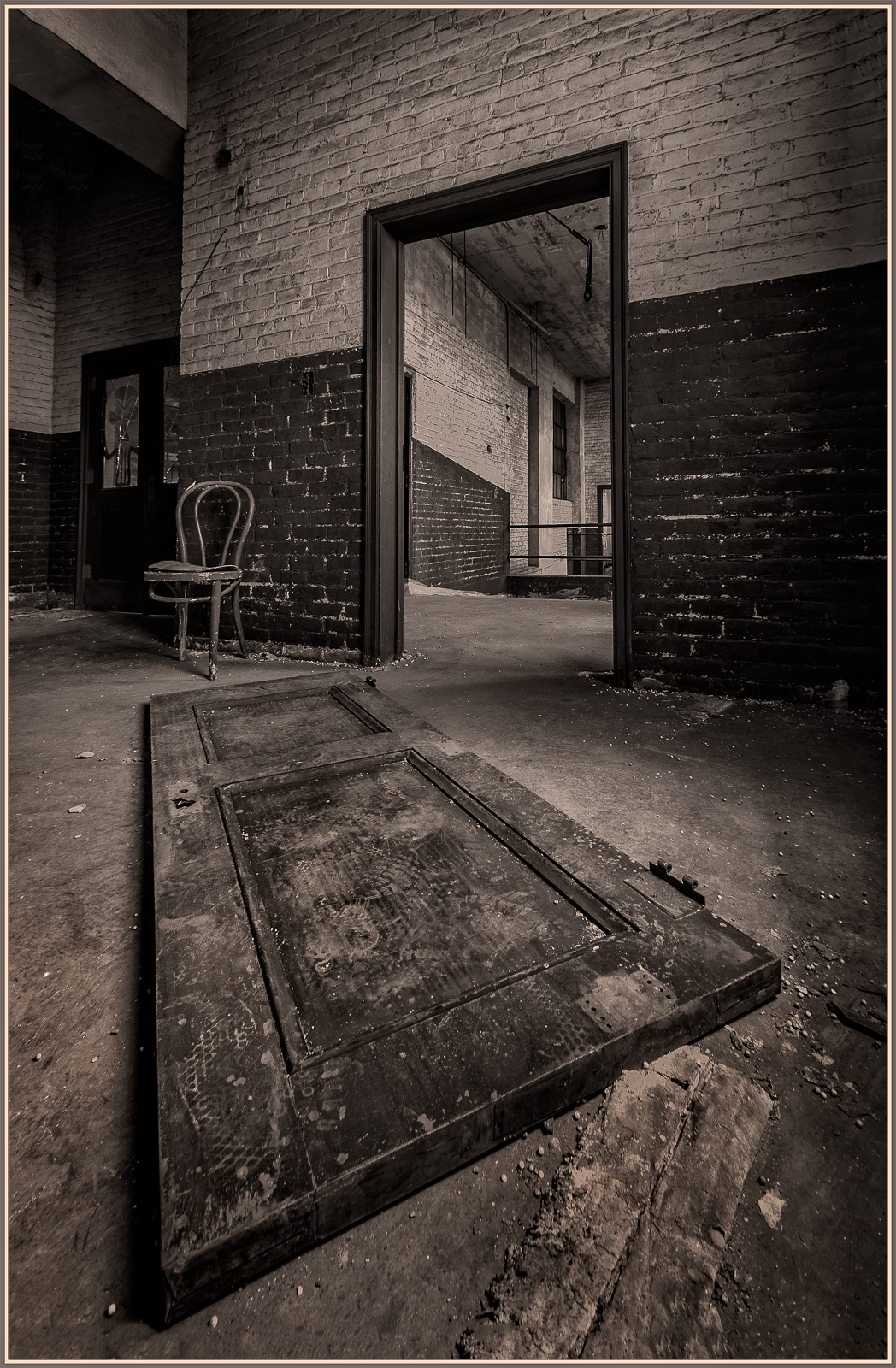 A warped door rests on the floor, framing a shadowy archway. A solitary chair whispers of forgotten tales and time's emb