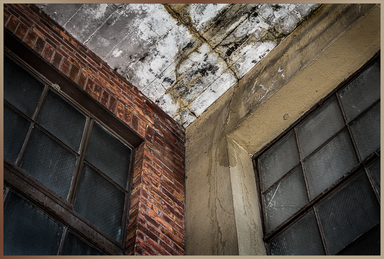 A close-up of weathered brick and concrete walls with large windows, showcasing decay and age.