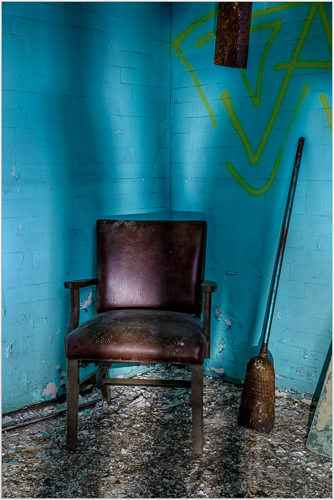 A worn brown chair against a turquoise wall with shadows and textures.