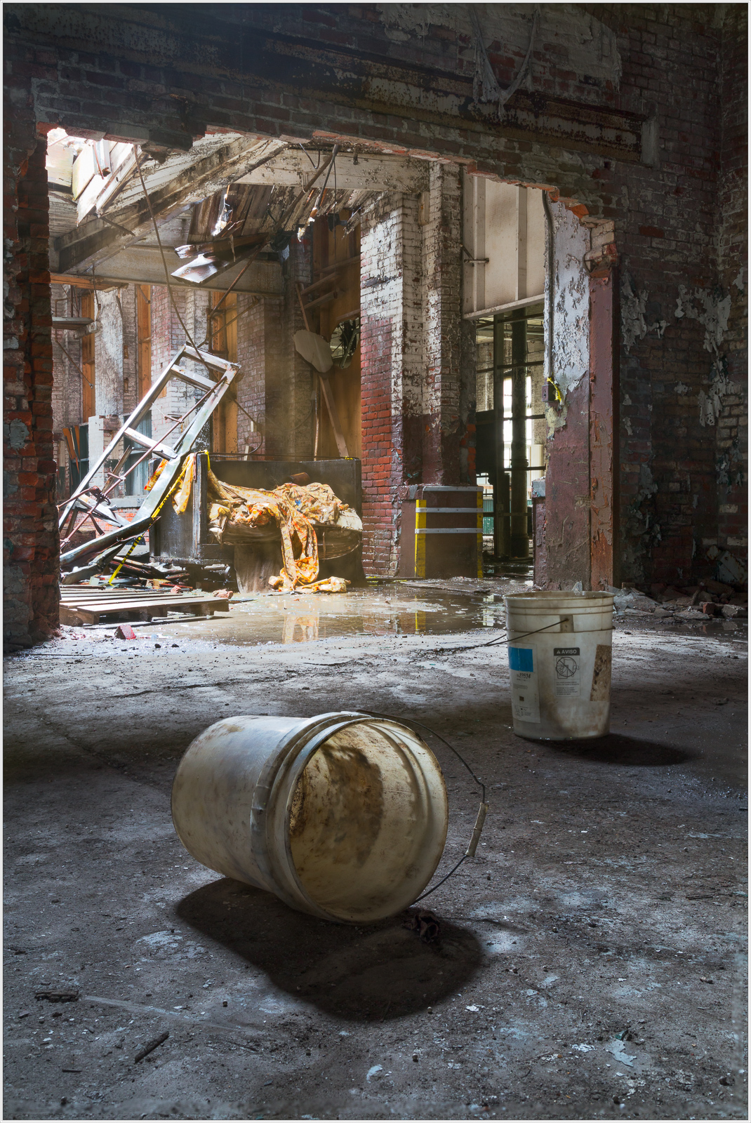 A desolate space with buckets scattered on cracked floors, remnants of past life linger in stillness.