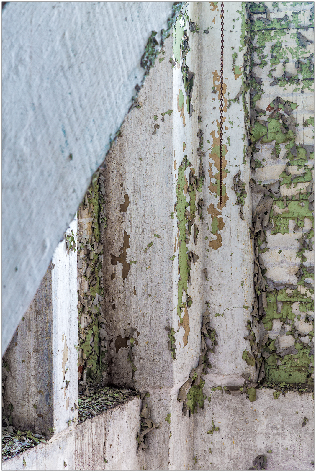 Peeling paint on white walls with green patches in an abandoned building.