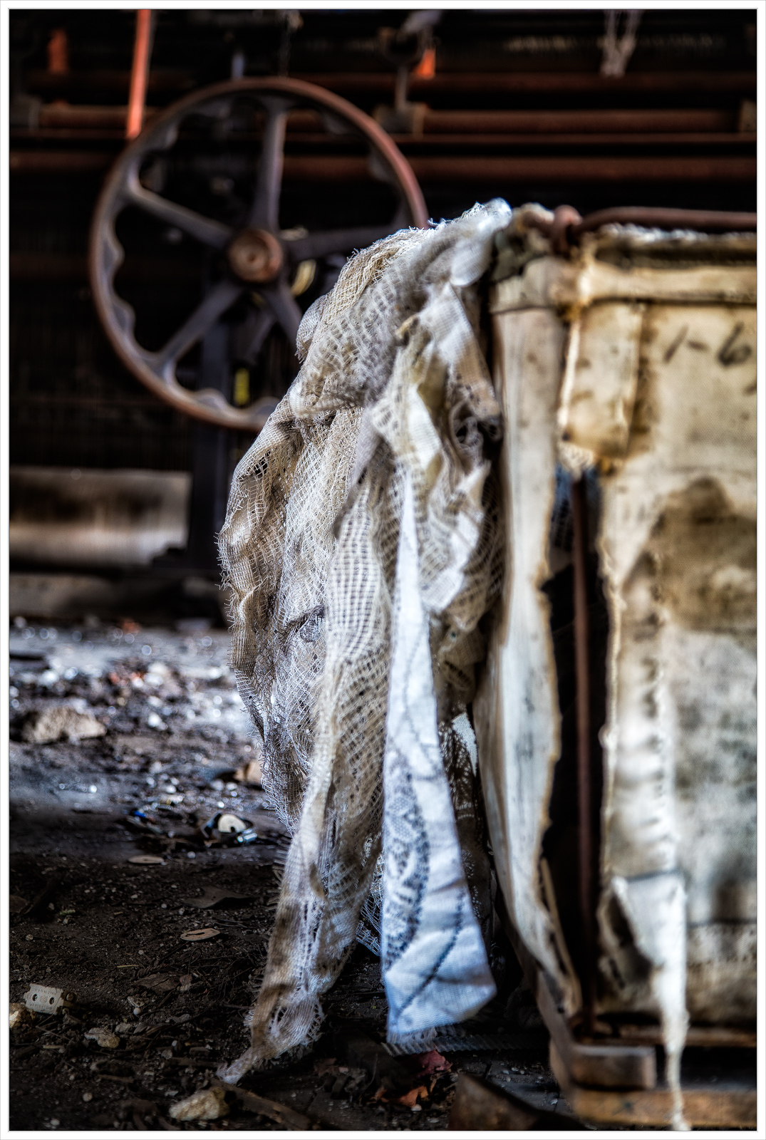 A weathered fabric drapes over a rusted structure, with shadows playing in the dim light.