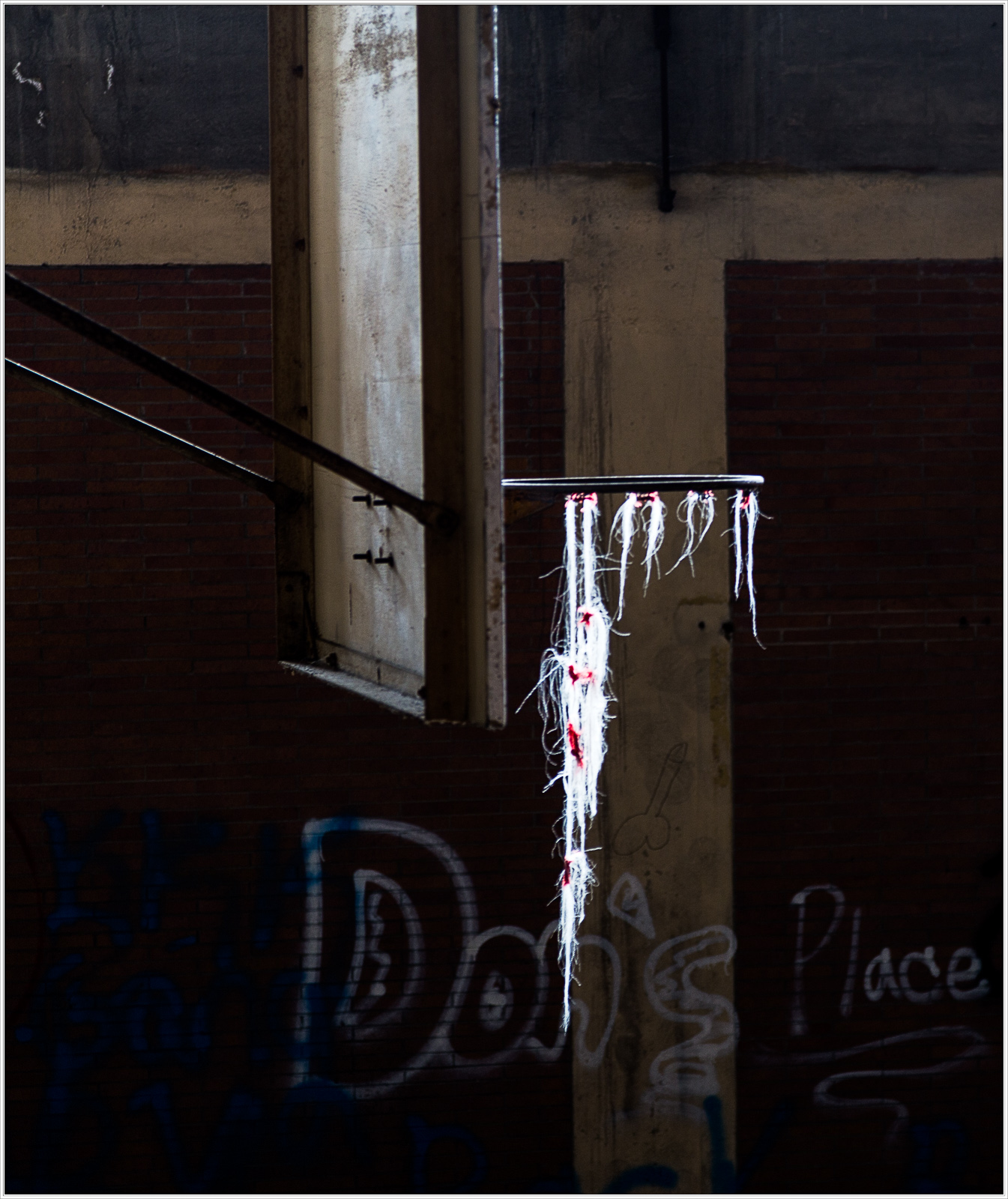 A broken window draped with threads of white and red against a backdrop of faded graffiti.