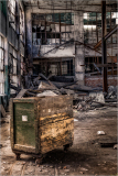 An old, weathered cart in an abandoned industrial space with debris and broken windows.