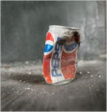 A crumpled can rests upon a silent, dusty floor, time's passage etched in its battered form.