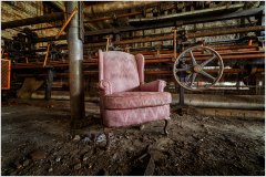 A lonely pink armchair amid rusted machinery and shadows; an eerie testament to forgotten times.