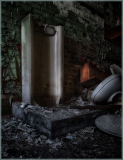 An abandoned shower stall amidst crumbling walls and scattered debris.