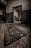 A warped door rests on the floor, framing a shadowy archway. A solitary chair whispers of forgotten tales and time's emb