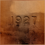 A weathered inion of the year 1927, surrounded by earthy textures.