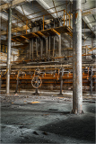 An abandoned industrial space reveals rusty machinery and a layered structure of pipes.