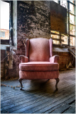 A worn pink chair in a dusty, dilapidated space; layers of peeling paint.