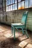 Abandoned teal chair in sunlight, showcasing wear and textures of the urban environment.