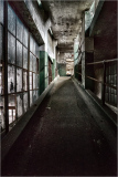 Abandoned corridor with worn walls, faint light filtering through dusty windows.