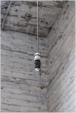 A close-up of an old light fixture hanging in a weathered wooden interior.