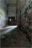 Interior view of an abandoned building with peeling walls and a dimly lit corridor.
