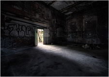 Dark, abandoned space with graffiti on walls, shadows creeping through a doorway.