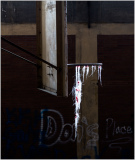 A broken window draped with threads of white and red against a backdrop of faded graffiti.