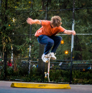 A skateboarder performs an impressive trick over a yellow rail in a lively park.