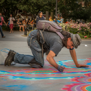 A man kneels on the ground, creating vibrant chalk art in a public space.