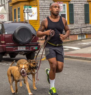 A man jogs with two energetic dogs, navigating a bustling street.