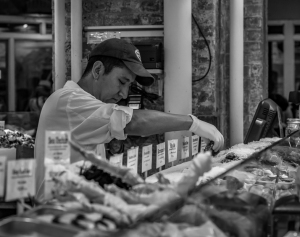 A chef skillfully prepares sushi at a bustling market, surrounded by fresh ingredients.