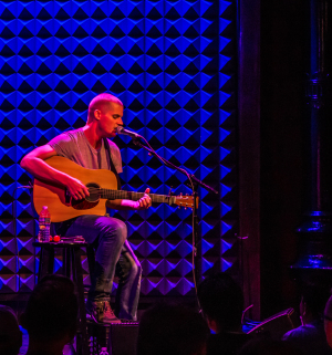 A musician strumming a guitar under vibrant blue lighting on stage.
