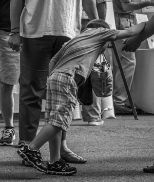 A kid in plaid shorts leans down, reaching for something on the ground.
