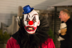 A colorful clown with a blue hat and dramatic makeup, grinning broadly.
