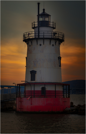 Tarrytown Lighthouse stands against a sunset, reflecting on the water's surface.