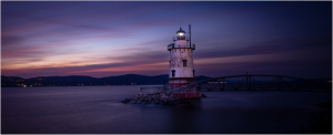 Tarrytown Lighthouse at dusk, surrounded by water and distant hills under a colorful sky.