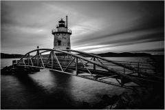 Black and white image of Tarrytown Lighthouse with a bridge over water.