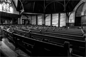 Abandoned church interior with rows of wooden pews and dramatic shadows.