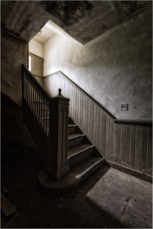 Staircase in a dimly lit abandoned building, shadows cast on faded walls.