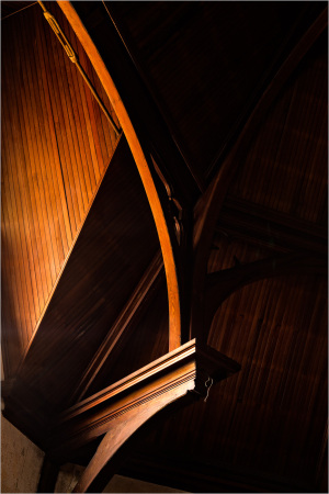 A grand wooden arch, resplendent and stoic, clutches the ceiling with grace.